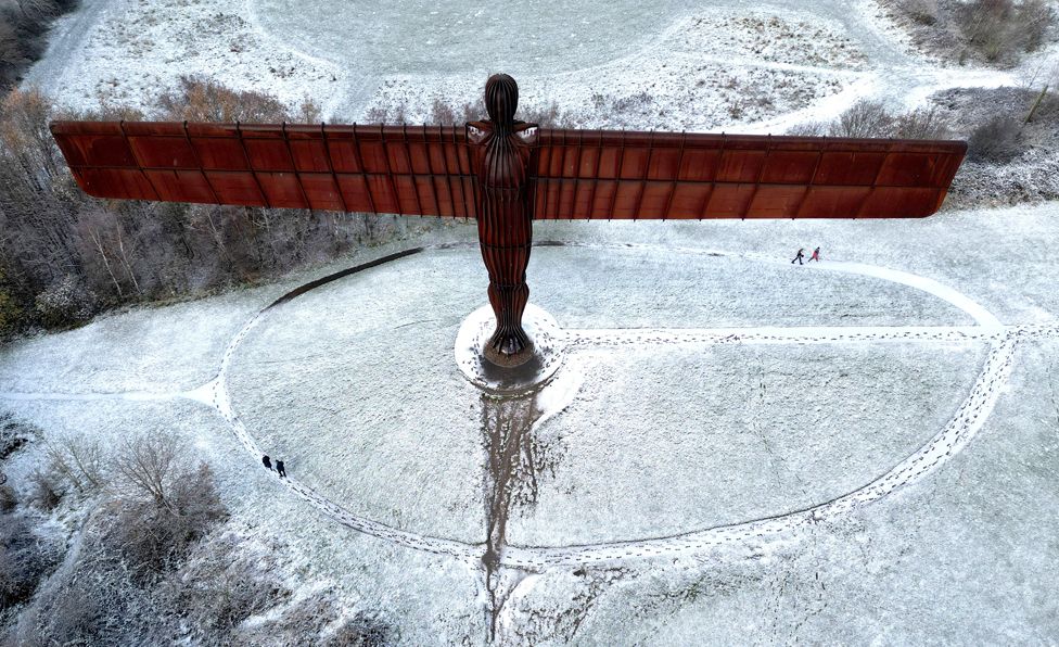 People walk next to Antony Gormley's Angel of the North as snow continues to fall in Gateshead, Britain, November 30, 2023.