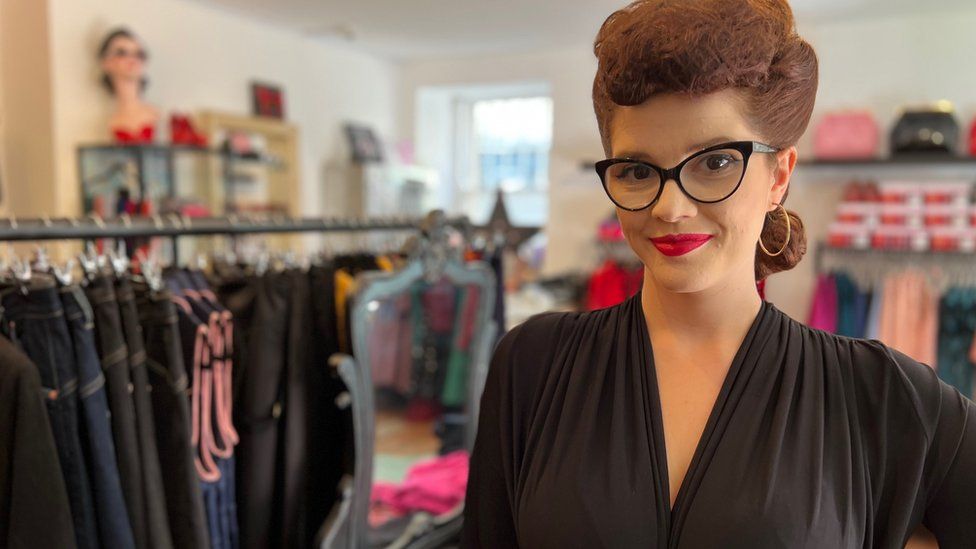 Sarah Wingrove smiling at camera in shop with clothes rail behind