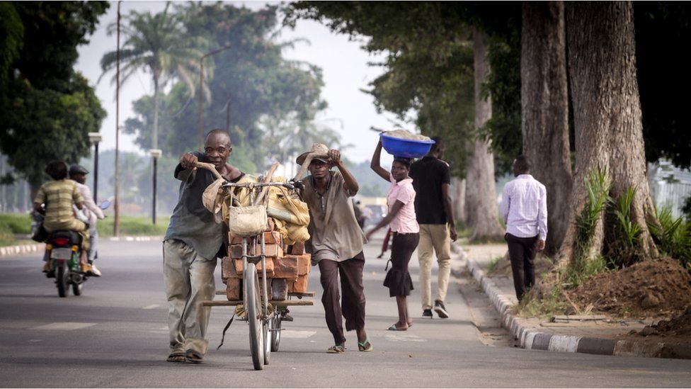 Men pushing a heavily laden bicycle on the streets of Kananga