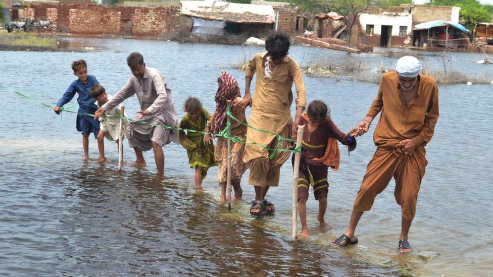 People wade through a flooded area in Sindh province