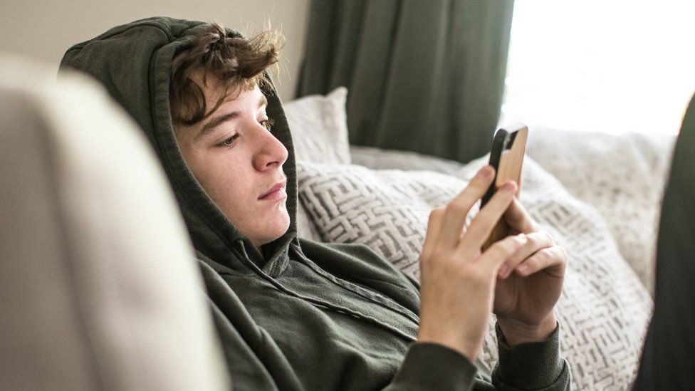 Stock image of a teenager sitting on the sofa looking at their phone
