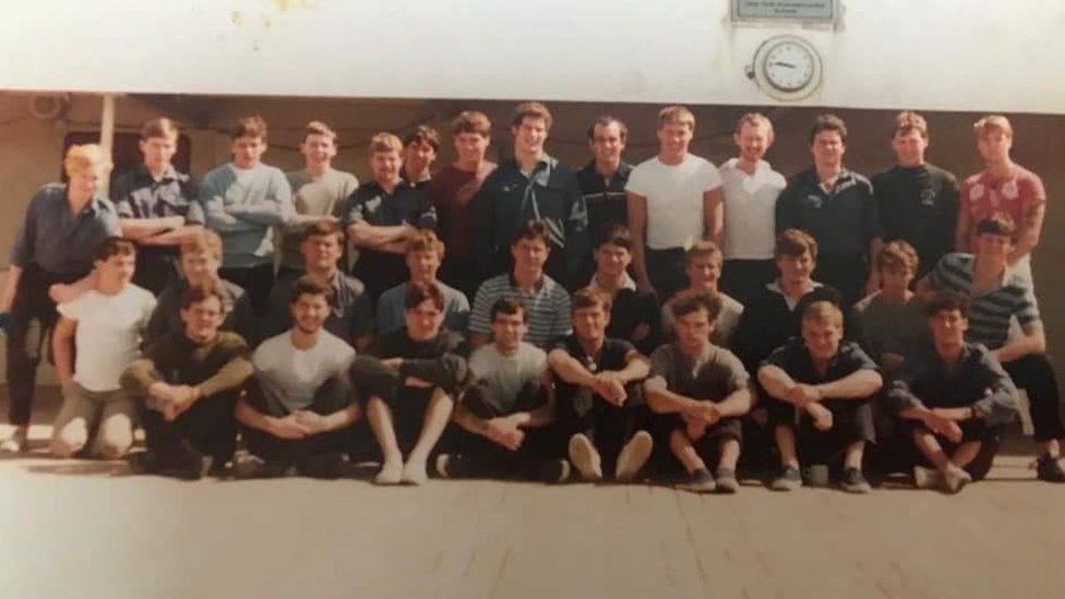 The crew of HMS Coventry who were rescued and are on board the QE2 on their way back from the Falklands. Mick is the fourth one from the left on the top row.