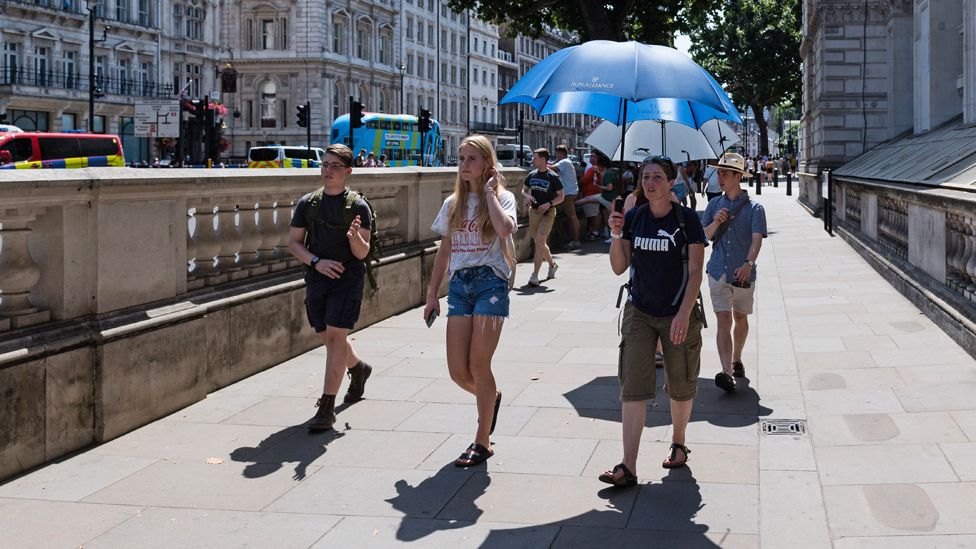 A group walk down the street with an umbrella up to shade them from the sun