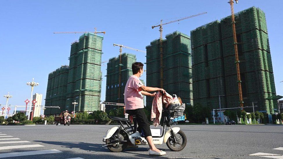 A woman rides a scooter past the construction site of an Evergrande housing complex in China's Henan province in September 2021.