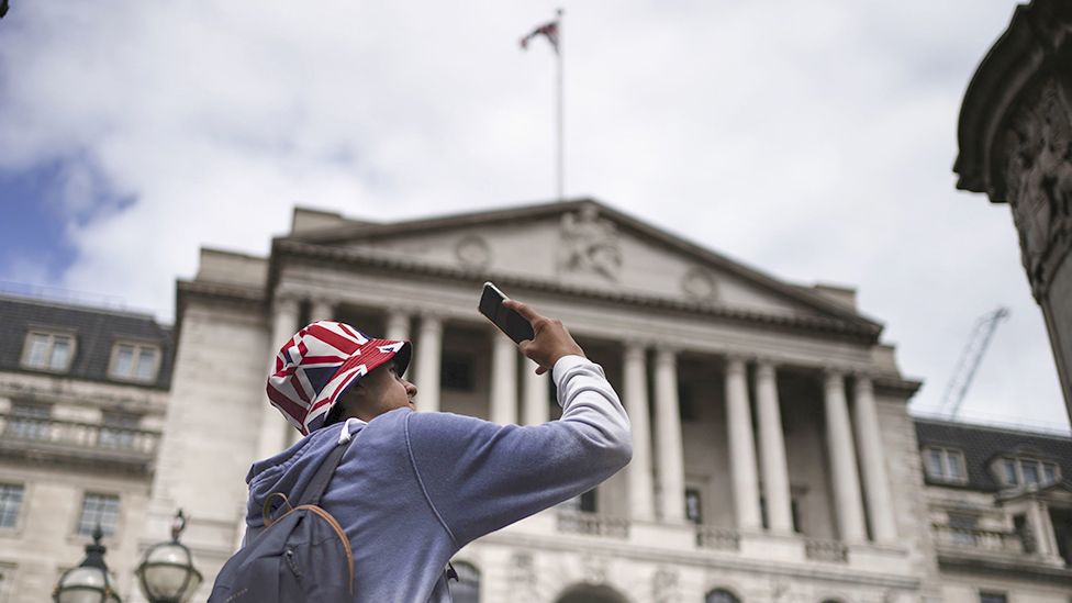 Общий вид Банка Англии в Лондоне 3 августа, на переднем плане человек, делающий снимок на мобильный телефон