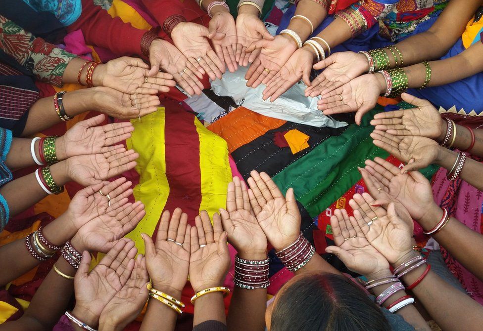 Women in a circle holding their hands out whilst surrounded by coloured cloth