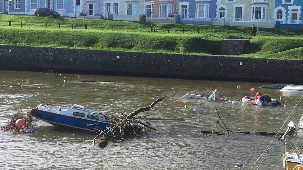 Boat in Aberaeron harbour covered in debris as people on another boat pull items from the water