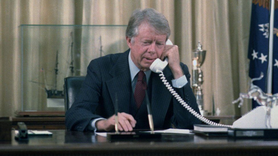 Jimmy Carter makes a phone call at his desk in the Oval Office