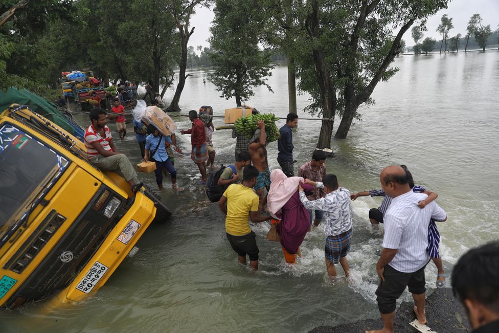 People wade past stranded trucks on a flooded street at Chhatak in Sunamganj, Sylhet, Bangladesh on June 22,2022.
