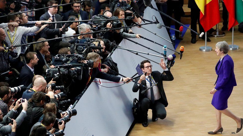 Theresa May walks towards a mob of cameras