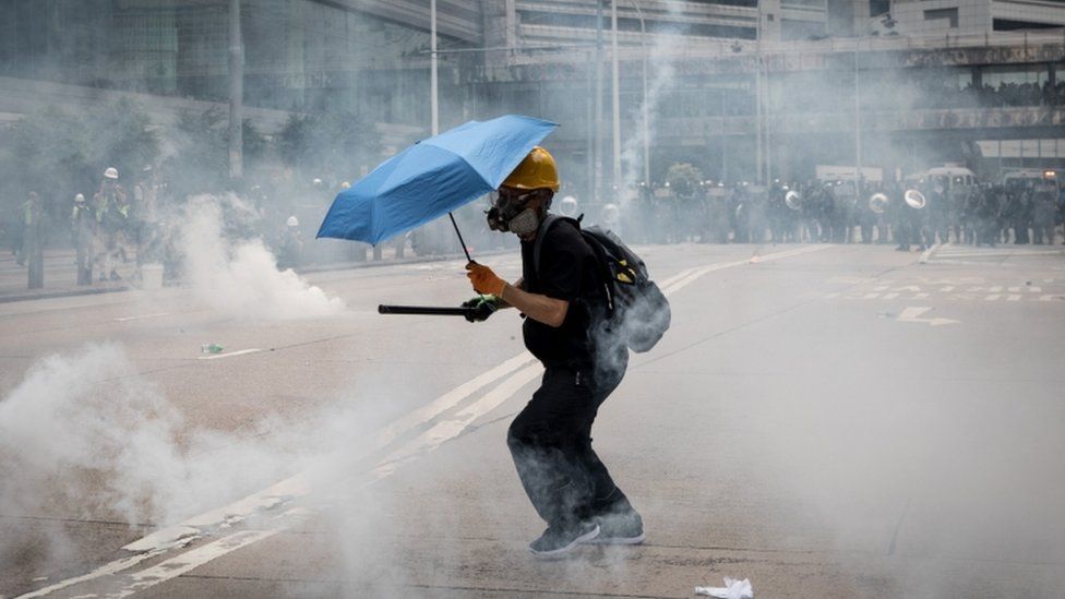 A lone protester wearing a gas mask and carrying an umbrella surrounded by tear gas in Hong Kong