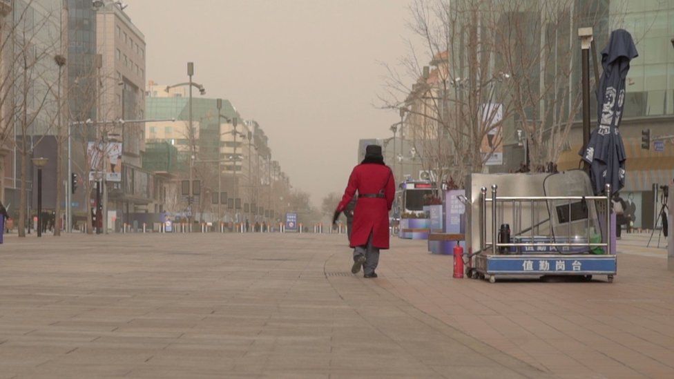 A guard in a red coat walks through an otherwise deserted shopping strip in Beijing