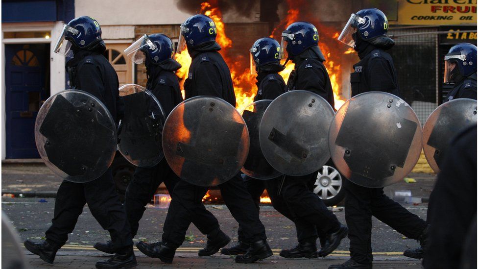 Police officers in riot gear near a fire in the street