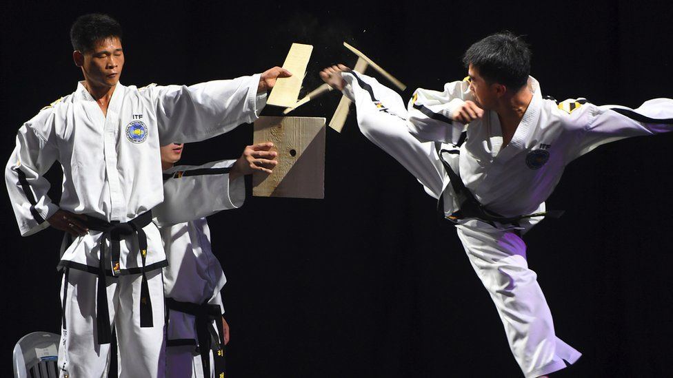 A man kicks through a wooden board during a taekwondo demonstration