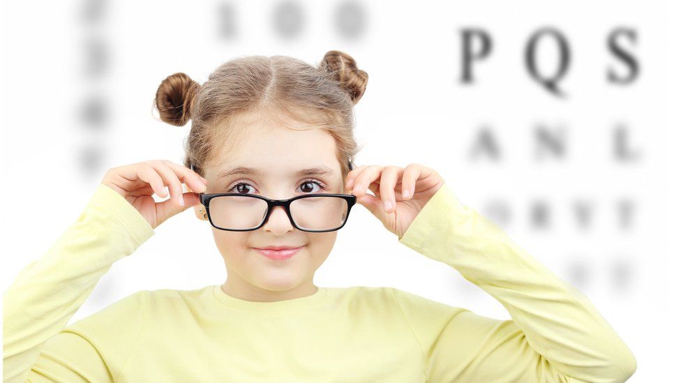 A girl in glasses in front of a row of letters
