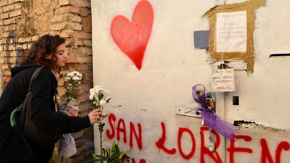 A young woman places flowers at the entrance of a sequestered derelict building in the San Lorenzo district of Rome