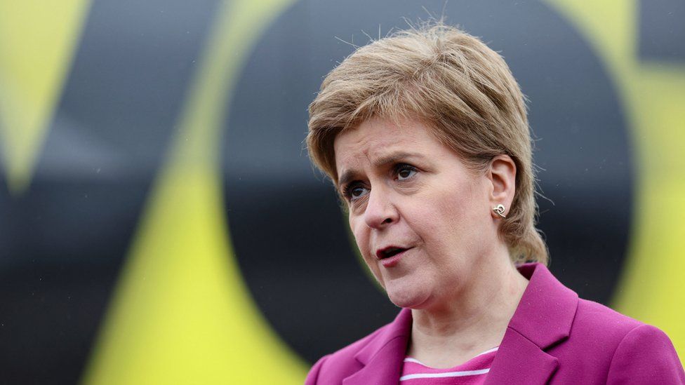 Nicola Sturgeon in a pink jacket, looking out of the frame with a serious expression