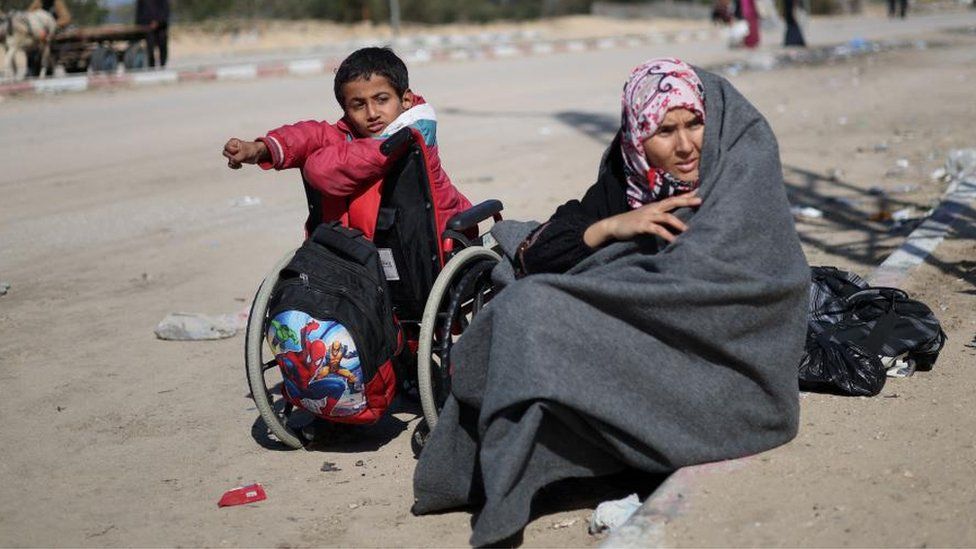 A Palestinian woman and child, fleeing Khan Younis, sit along the road amid a move towards Rafah
