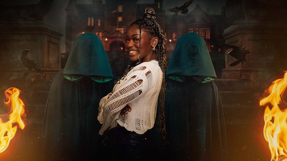 Jasmine's promotional photo for The Traitors. Jasmine is a 26-year-old black woman with long braids. She wears a long-sleeved crochet cream top. She stands facing right, arms folded, and turns her head to smile at the camera. She is flanked by two cloaked traitors in front of the Scottish castle where the series is filmed and flames have been added for dramatic effect