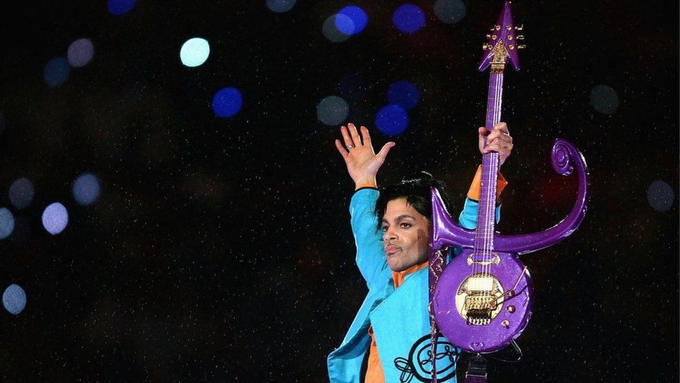 Prince holds a guitar shaped like the symbol that he took as his name in 1993
