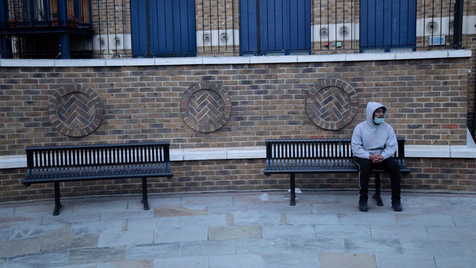 Man wearing face mask sitting on bench in Shoreditch, London during Coronavirus crisis