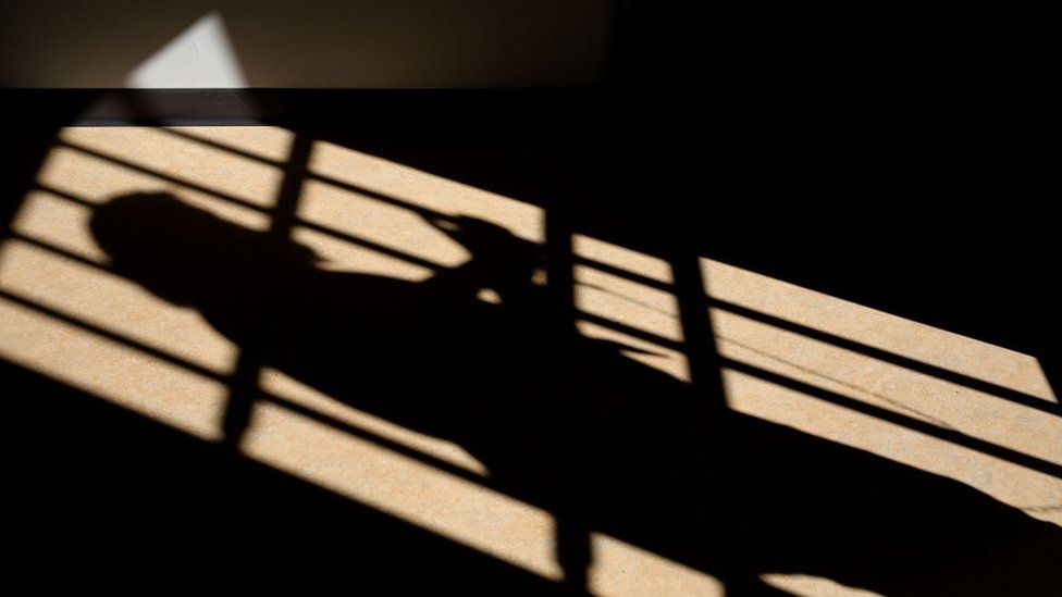 Shadow of barred gate and prison officer