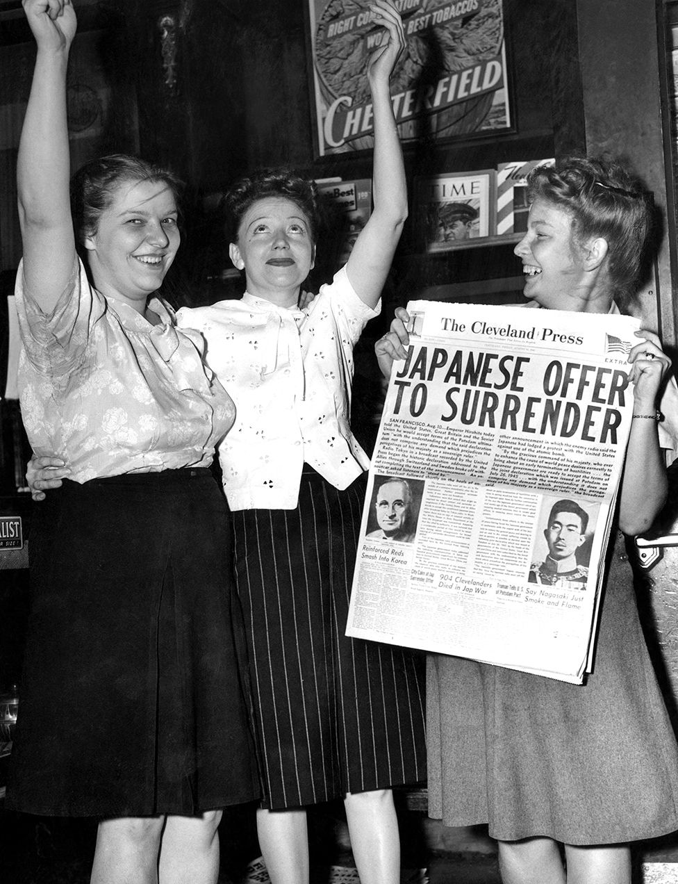 Women hold a newspaper and raise their arms