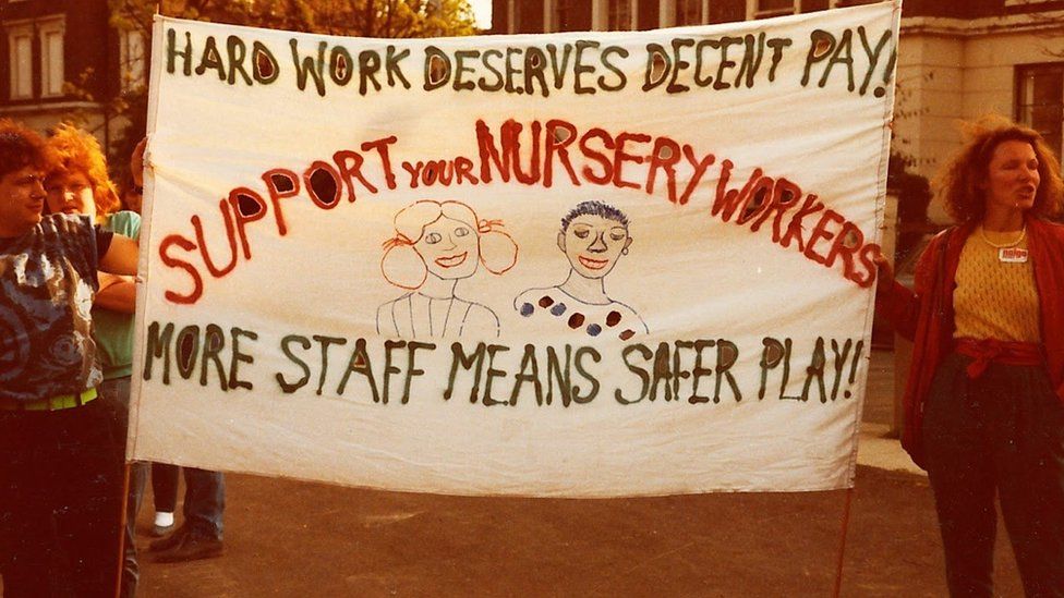 Strikers hold a white banner saying 'hard work deserves equal pay' and 'more staff means safer play'