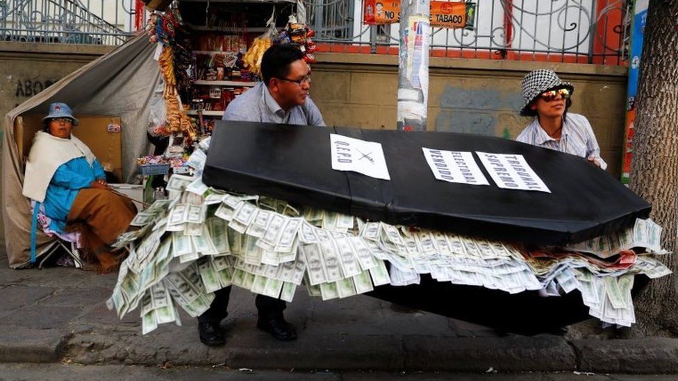 Two people carry a papier-mache coffin filled with paper bills in La Paz