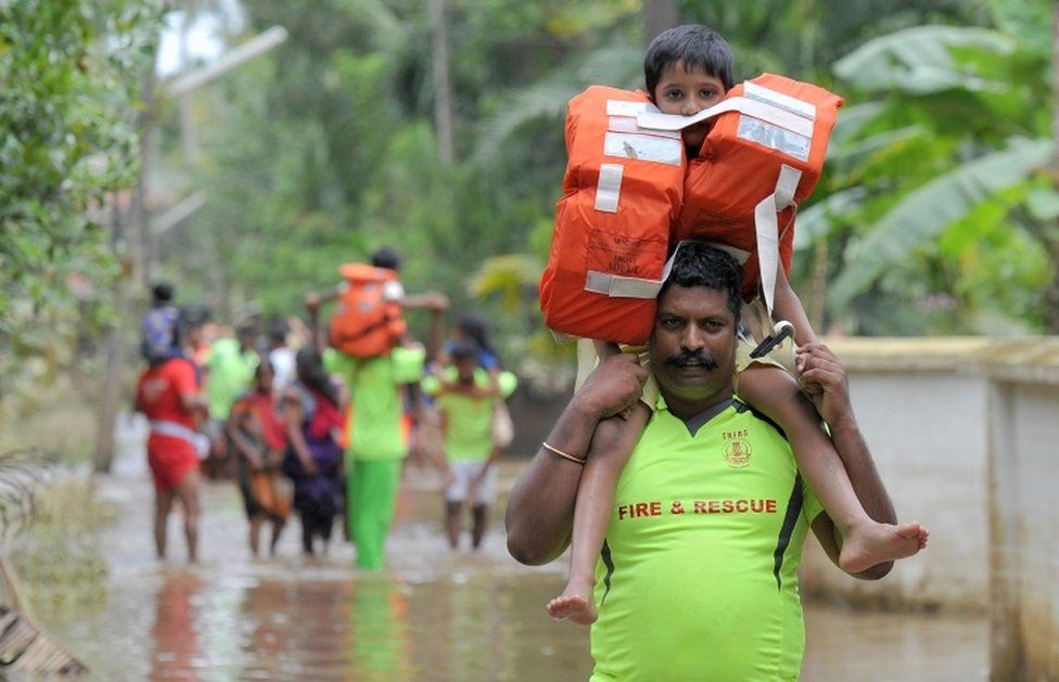 Fire service personnel carry children on their shoulders through floodwaters during a rescue operation in Annamanada village, in Kerala