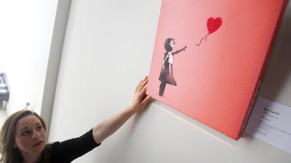 A Bonhams' employee adjusting a version of Banksy's Balloon Girl