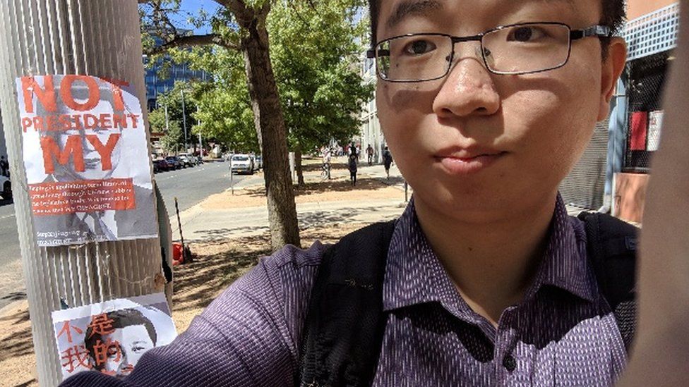 Wu Lebao stands next to a poster saying "not my president" at the Australian National University