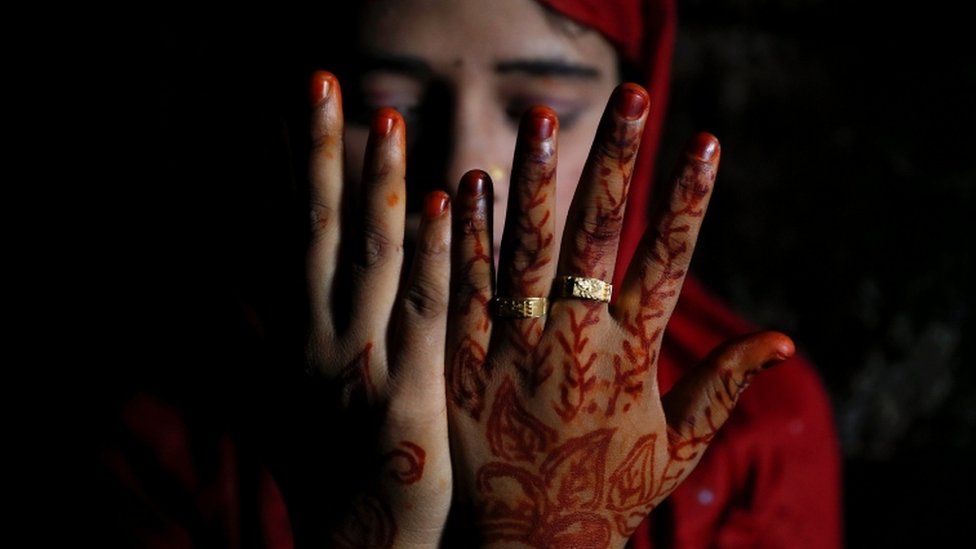 A Rohingya refugee holds henna-decorated hands up to cover her face