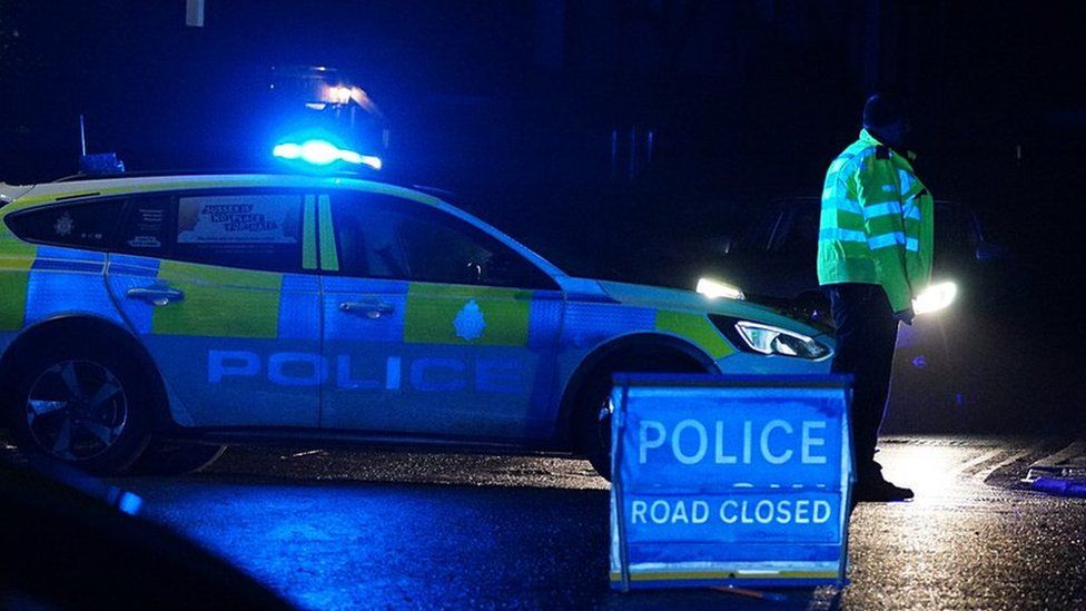 A police officer and police car with a road closure sign at night