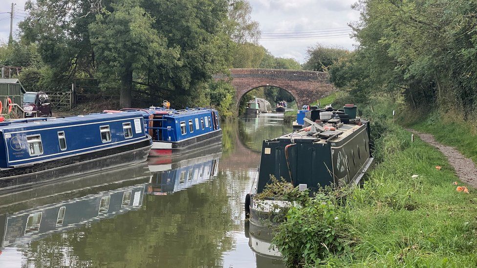 Three canal boats moored on the Kennet and Avon canal in the Pewsey Vale with a bridge in the distance
