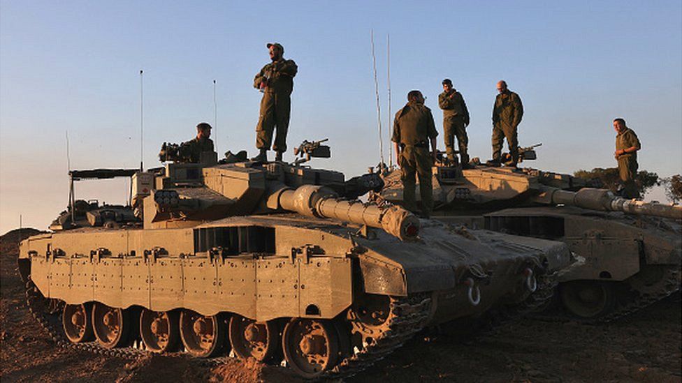 Israeli soldiers stand on tanks deployed on the southern border with the Gaza Strip on 29 November 2023