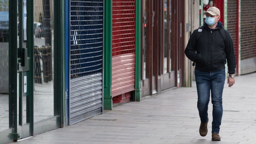 Man wearing face mask walking past shuttered shops in Cardiff