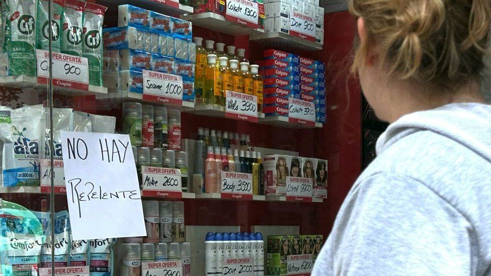 A woman stands in front of a 'no repellent' sign at a supermarket