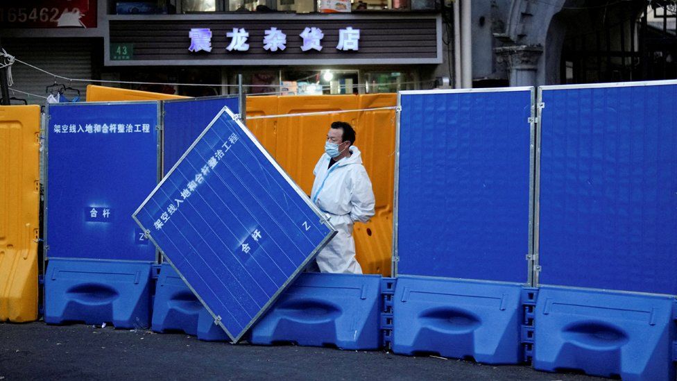 A worker in a protective suit keeps watch next to barricades set around a sealed-off area of Shanghai