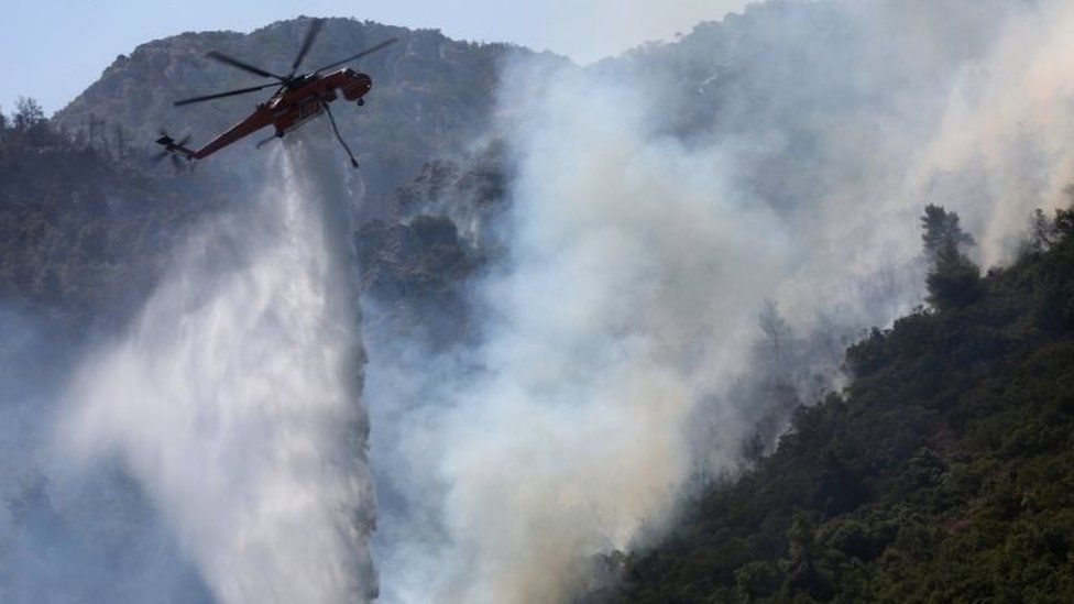 A firefighting helicopter douses a wildfire near Athens