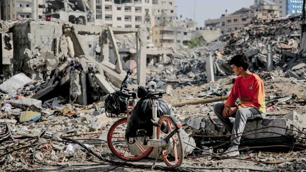A Palestinian youth sits next to his bicycle amid the rubble of destroyed buildings in Gaza City on the northern Gaza strip on 24 November 2023.