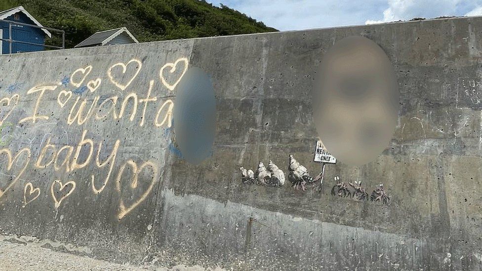 Graffiti on sea wall at Cromer, including 'I want a baby' and hearts in spray paint, with some spraypaint on part of the Banksy mural
