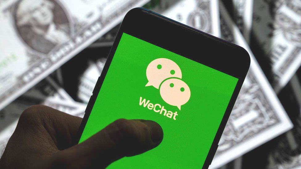 The WeChat logo seen displayed on a smartphone with United States dollar currency in the background.