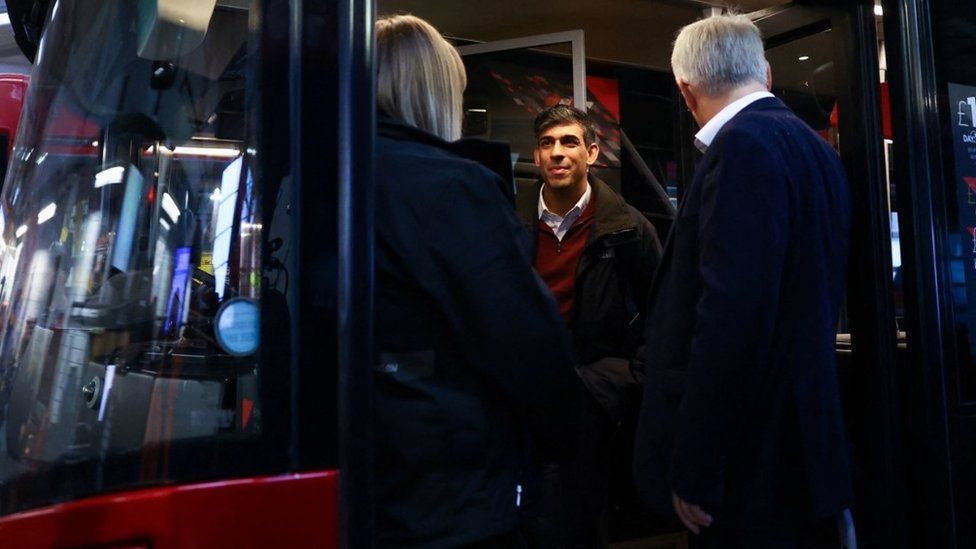 Rishi Sunak talks to people while standing on the steps of a red bus