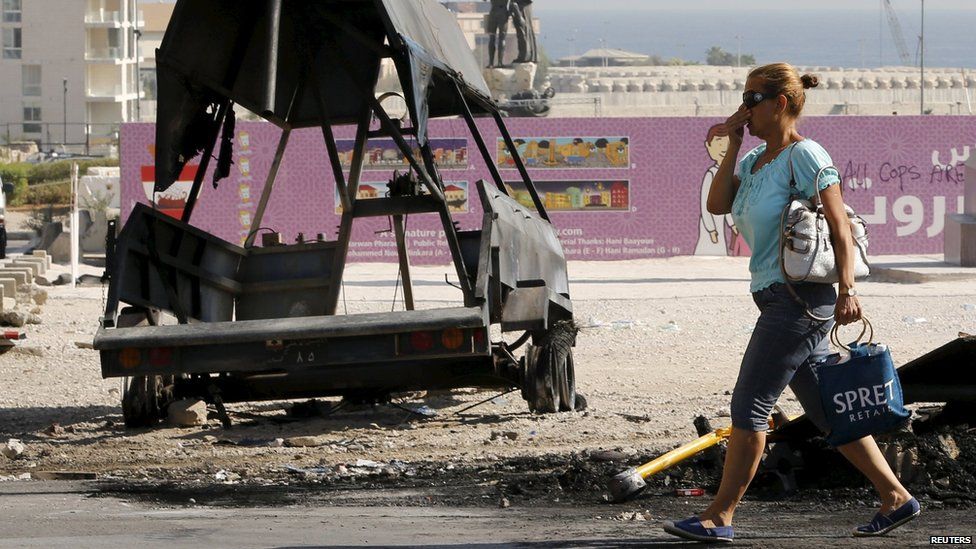 A woman holds her nose as she walks past a burnt-out police vehicle in central Beirut (24 August 2015)