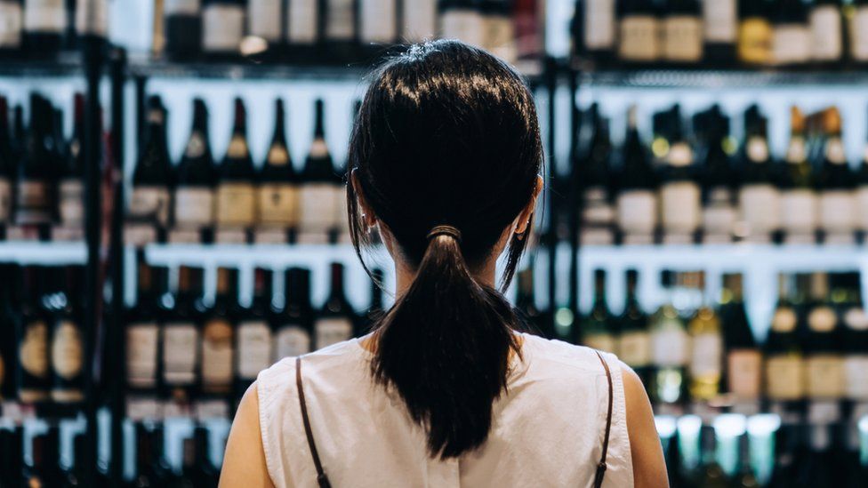 A woman standing in front of a shelf filled with wine bottles