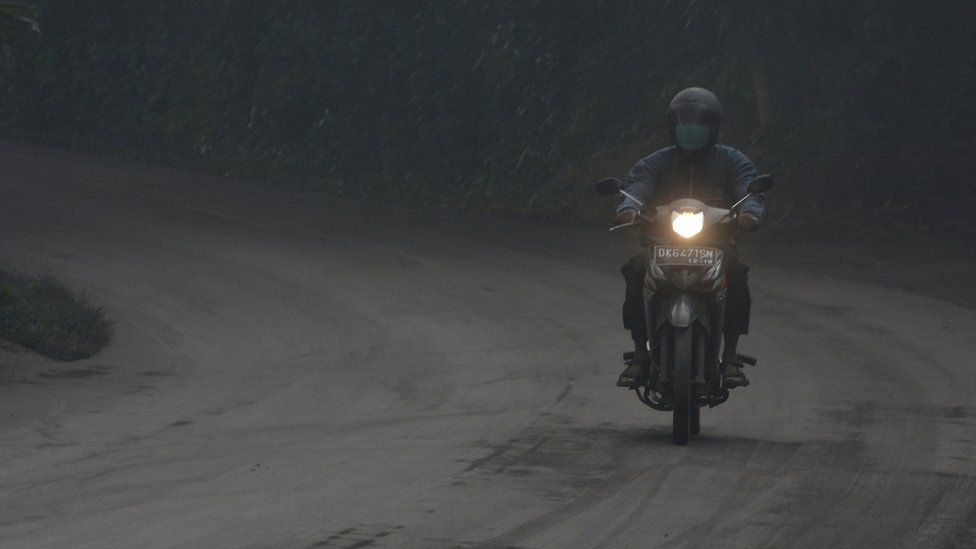 A motorist rides his motorbike during a shower of ash and rain from Mount Agung