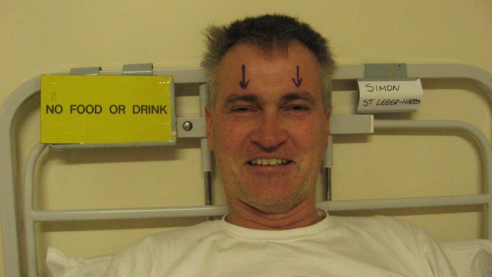 Man in hospital bed with two arrows drawn on above his eyes