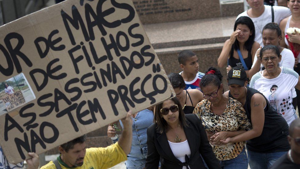 Man holds sign that reads "The sadness of mothers of children killed, doesn't have a price" at funeral for Eduardo Victor. 30 Sept 2015