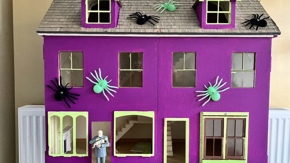 A purple haunted mansion made from an old doll house. There are green and black spiders glued all over it